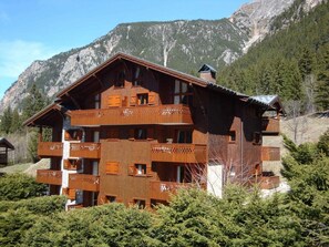 Ein mehrstöckiges Holzchalet mit Balkonen vor einer Bergkulisse.