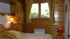 Una habitación de cabaña de madera con una cama, una mesita de noche con lámpara y una ventana con cortinas.
