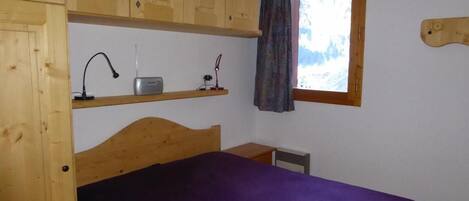A room with a bunk bed, a desk with a lamp, a window with a view, and a wooden headboard.