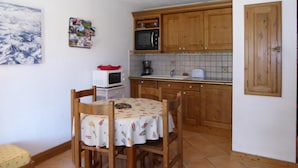 Une cuisine compacte dotée de meubles en bois, d’un four à micro-ondes, d’une machine à café et d’une table recouverte d’une nappe.