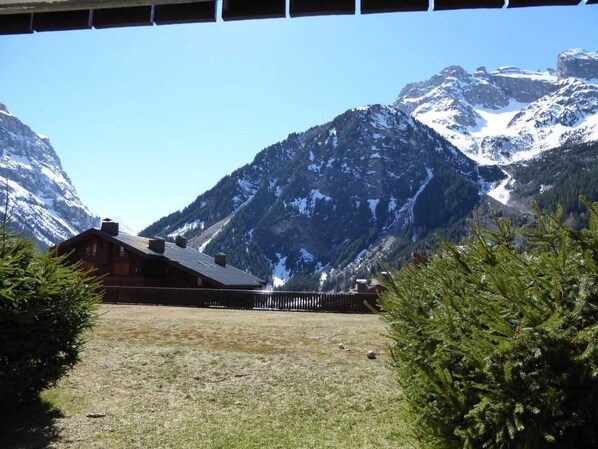 A mountain lodge with a wooden exterior, a fenced yard, and a clear view of snow-capped mountains.