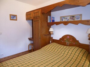 A bedroom with a wooden bed, a nightstand, a shelf with books, and a door.