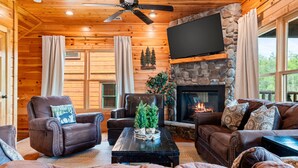 L’intérieur chaleureux d’un chalet avec une cheminée en pierre, des meubles en cuir et un ventilateur de plafond.