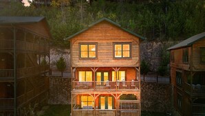 Un chalet en bois à deux étages, doté d’un balcon, de fondations en pierre et d’un mur de soutènement en pierre.