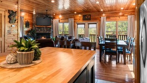 L’intérieur d’un chalet en bois comprend un coin repas, des sièges, une cheminée et un téléviseur fixé au mur.