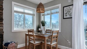Un comedor con una mesa y sillas de madera, una lámpara colgante y un ventanal con persianas.