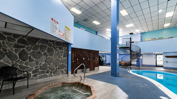 Un área de piscina con jacuzzi, pared de piedra y una escalera que lleva a niveles superiores.