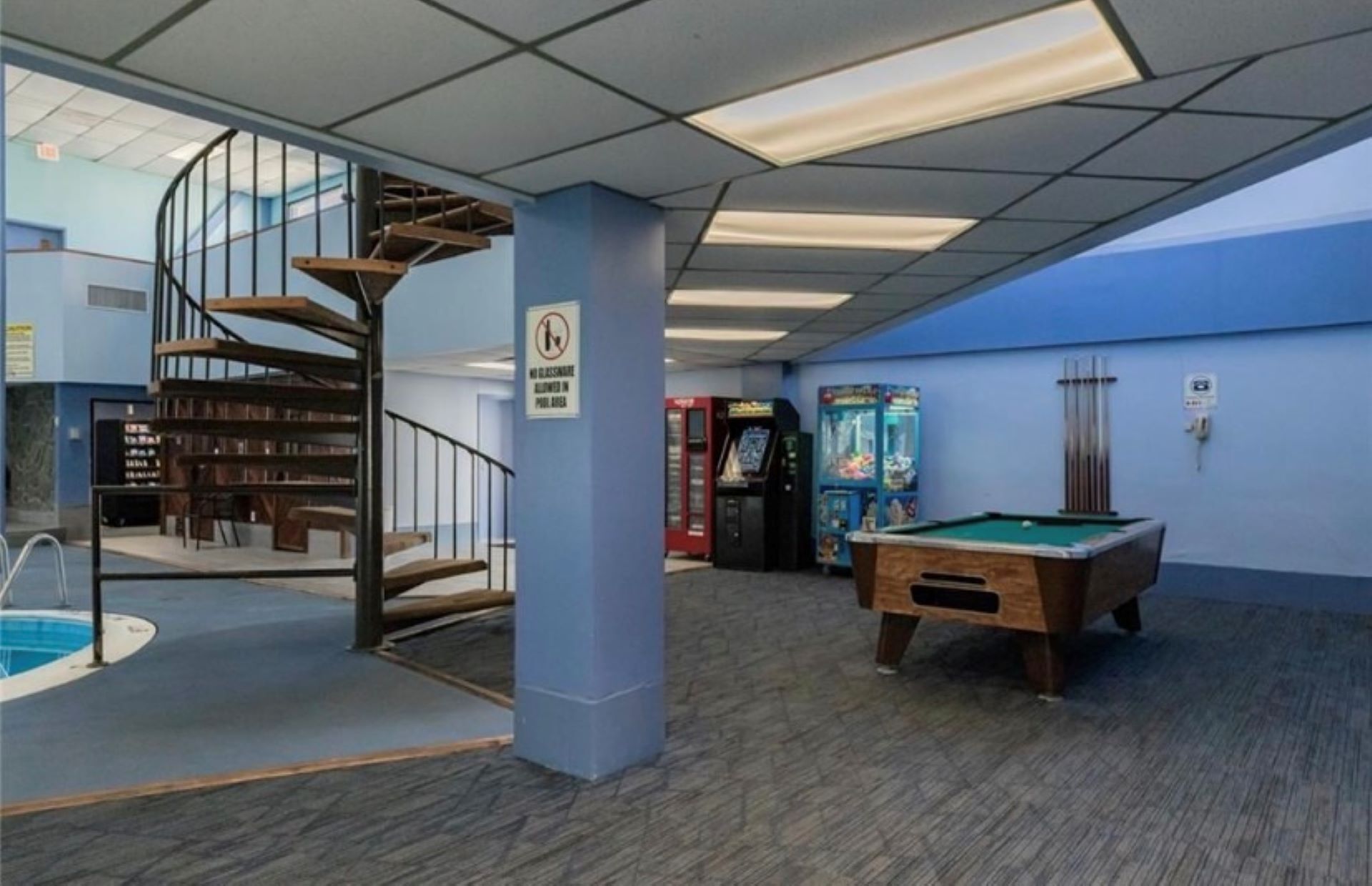 A pool area with a spiral staircase, a pool table, and arcade machines.