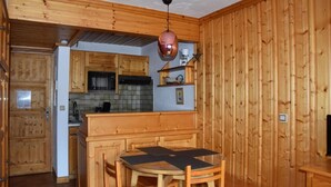 Eine kompakte Küche mit Holzausstattung, einem Esstisch mit Stühlen und einer hängenden Pendelleuchte.
