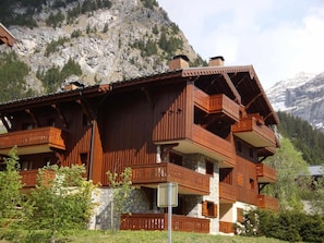 A wooden chalet with multiple balconies, set against a mountainous backdrop.