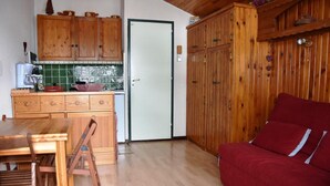 A compact living space with a wooden dining table, a red sofa, and a kitchen area with wooden cabinets and a tiled backsplash. - 3rd floor, balcony, tv, ski locker, 22m², Pralognan-la-Vanoise (Pralognan-la-Vanoise)