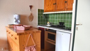 A compact kitchen with wooden cabinets, a small refrigerator, and a countertop with a coffee maker and a basket. - 3rd floor, balcony, tv, ski locker, 22m², Pralognan-la-Vanoise (Pralognan-la-Vanoise)