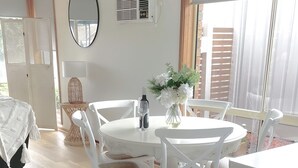 Una zona de menjador blanca amb taula rodona, cadires blanques, un vas amb flors i una ampolla de vi.