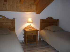Une chambre avec deux lits simples, une table de chevet avec une lampe et des poutres en bois au plafond.