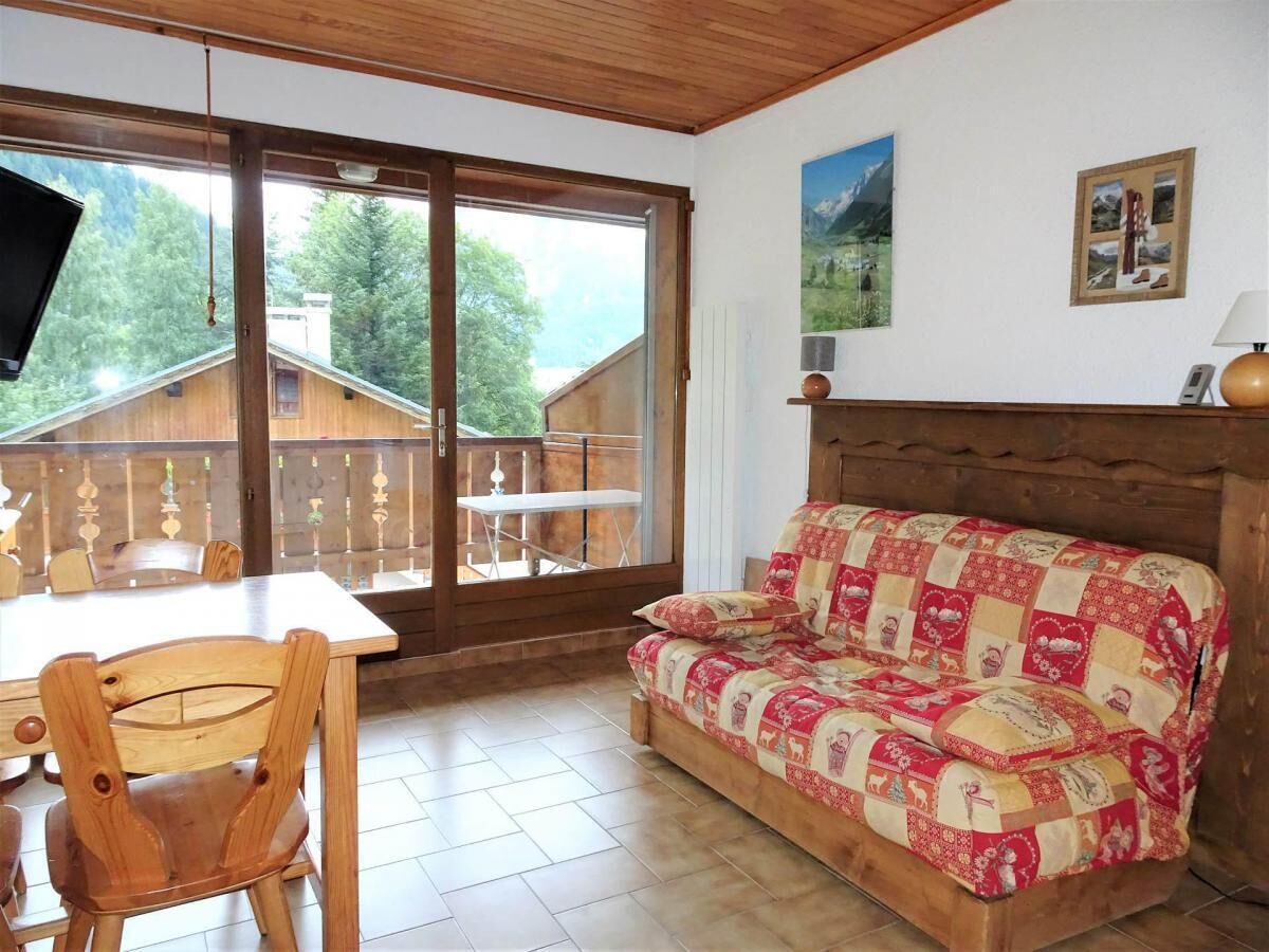 Una habitación acogedora con un sofá de madera, una mesa de comedor con sillas y un gran ventanal que ofrece vistas a una cabaña de madera y árboles.