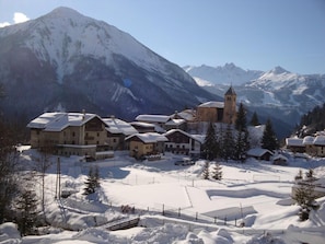 A snow-covered village with wooden buildings and a church, surrounded by mountains.