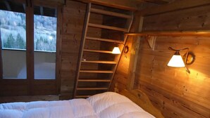 Une chambre aménagée dans une cabane en bois, avec un lit, une échelle et deux lampes fixées au mur.
