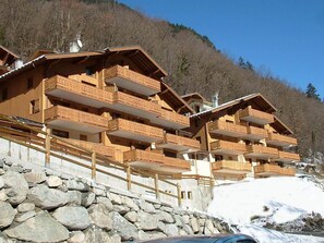 Un chalet en bois à plusieurs étages, doté de balcons, qui se dresse sur un fond de paysage montagneux.