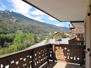 A balcony with heart-shaped cutouts, overlooking a mountain village with houses and a road.