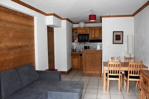 A compact living space with a sofa, dining table, chairs, wooden cabinets, a microwave, and a red hanging light fixture. - 1st floor, balcony, tv, ski locker, 40m², Courchevel (Bozel)