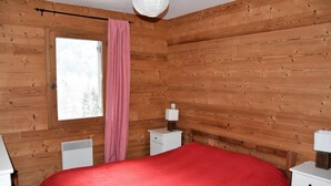 Ein Zimmer mit Holzwänden, einem Bett, einem Fenster, einem Heizkörper und einem Nachttisch mit Lampe.