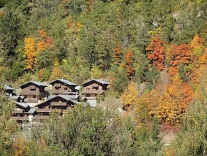 A cluster of wooden cabins with multiple stories and balconies, surrounded by dense forest with autumn foliage. - 1st floor, balcony, tv, ski locker, 40m², Courchevel (Bozel)