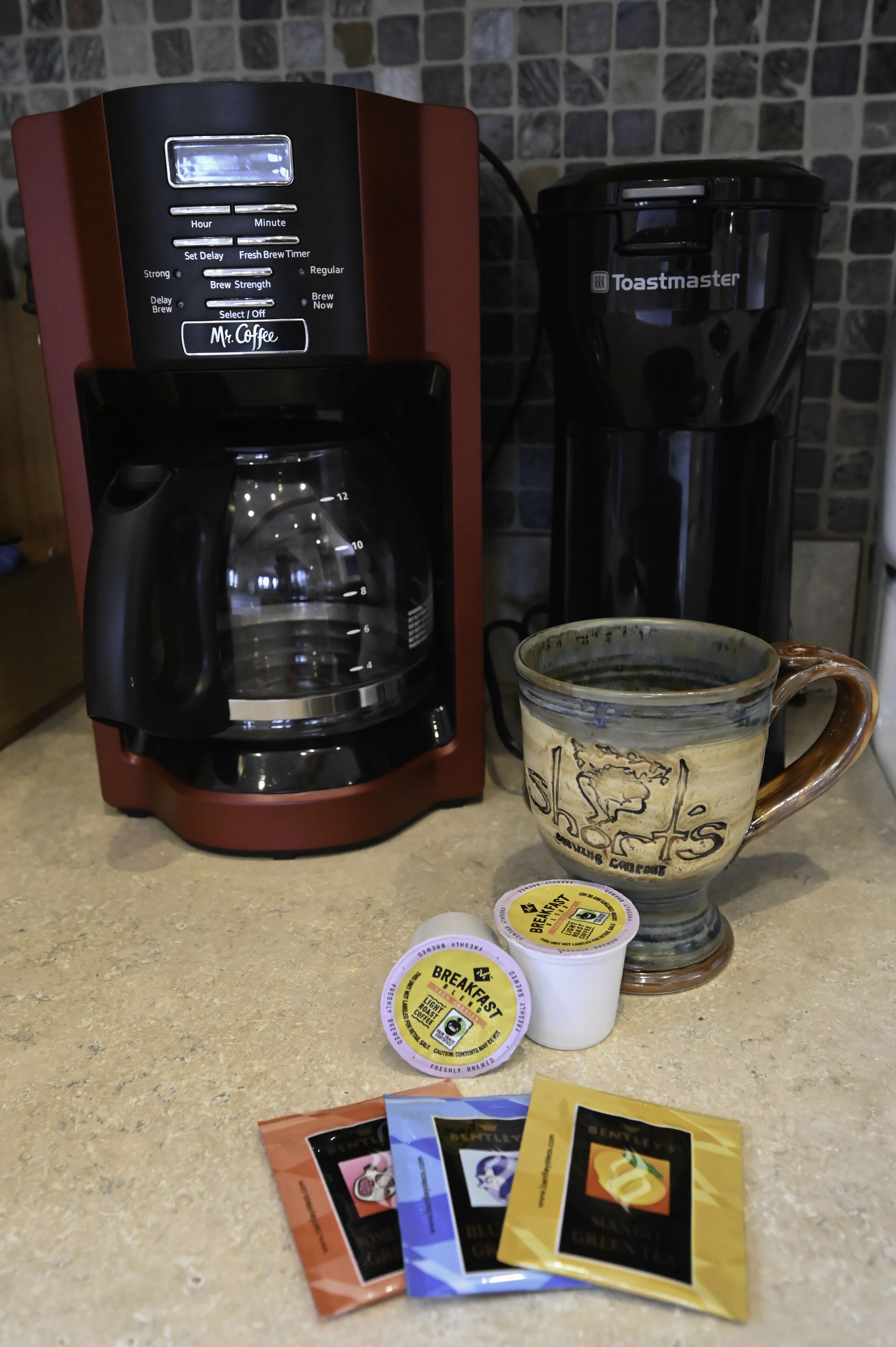 Uma cafeteira, uma caneca e cápsulas de café em uma bancada de cozinha.