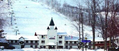 Ein Hotel mit einem zentralen Turm, zahlreichen Fenstern und einer Skipiste im Hintergrund.