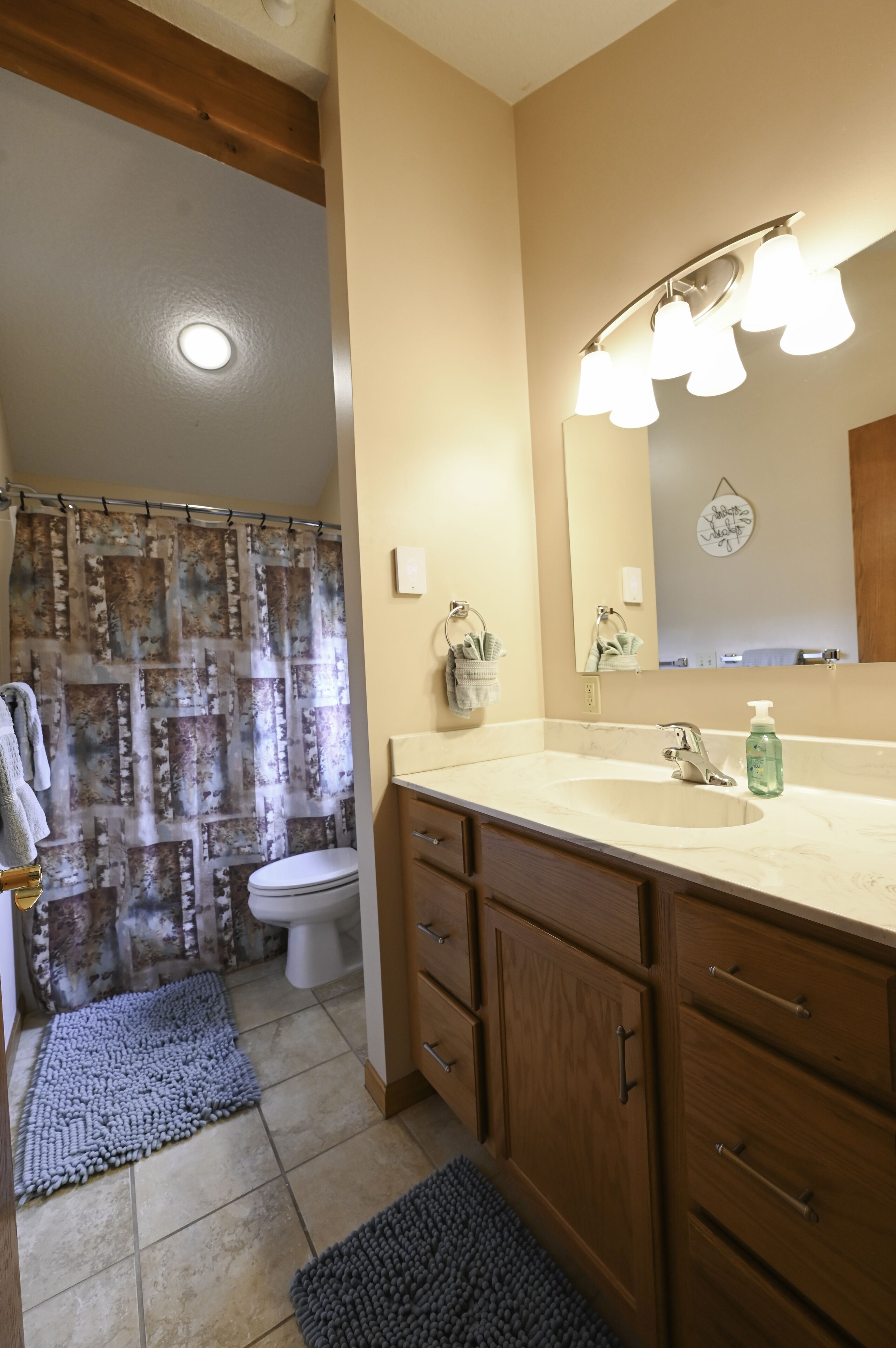 A bathroom with a shower curtain, toilet, sink, mirror, and wooden cabinets.