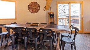 A dining area with a wooden table and chairs, a wall clock, and a view through a glass door. - Chalet, wifi, 50m from ski slopes, sauna, balcony, fireplace or stove, parking, tv, ski locker (Bellentre)