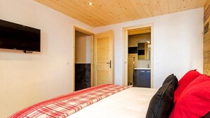 A bedroom with a bed, a TV mounted on the wall, and a wooden ceiling. - Chalet, wifi, 50m from ski slopes, sauna, balcony, fireplace or stove, parking, tv, ski locker (Bellentre)