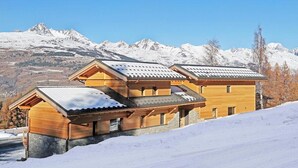 A wooden chalet with a sloped roof and stone foundation, set against a snowy mountain backdrop. - Chalet, wifi, 50m from ski slopes, sauna, balcony, fireplace or stove, parking, tv, ski locker (Bellentre)
