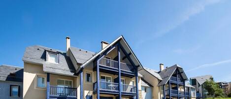 A row of modern, two-story townhouses with balconies, set in a sunny, grassy area.