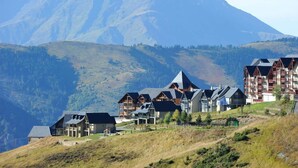 A mountain resort with chalet-style buildings, a ski lift, and a view of the surrounding mountains.