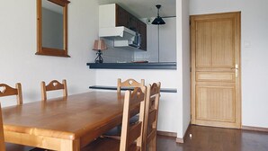 A dining area with a wooden table and chairs, a kitchen with cabinets and a microwave, and a wooden door.