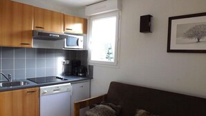 Cocina compacta con armarios de madera, microondas integrado y lavavajillas. Hay una ventana que proporciona luz natural y un cuadro en la pared.