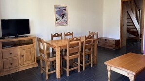 A dining area with a wooden table and chairs, a television on a wooden cabinet, and a poster on the wall.