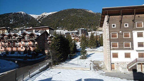 A snow-covered mountain town with traditional chalet-style buildings, a stone building with multiple windows, and a clear view of the mountains in the background.