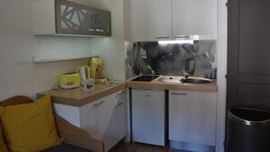 A compact kitchen with white cabinets, a sink, a small countertop, and a trash bin.