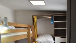 A bunk bed room with a wooden floor, a desk, and a wardrobe with multiple shelves.