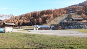Zona montañosa rural con un pequeño albergue, un muro de piedra y un automóvil estacionado cerca de un letrero de madera.