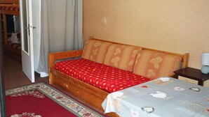 Una cama individual con colcha de diseño rojo y beige, cabecera de madera y mesita de noche con lámpara.