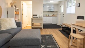 A compact living space with a grey sofa, a small wooden table, and a kitchenette area. - Welcoming Studio Walk to Palisades Resort & Lifts (Olympic Valley)
