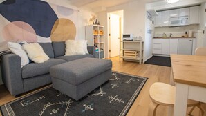 A modern living room with a grey sofa, ottoman, and a black rug with geometric patterns. A wooden dining table with a chair is visible. - Welcoming Studio Walk to Palisades Resort & Lifts (Olympic Valley)