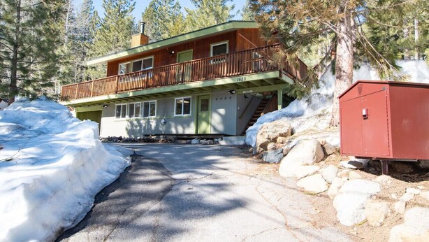 En toetages hytte med balkon, omgivet af sne og træer.