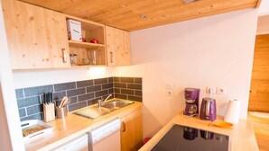 Una cucina compatta con mobili in legno, zoccolo paraschizzi in piastrelle nere, lavastoviglie integrata, macchina da caffè e un tablet sul ripiano.