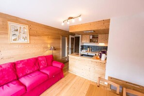 Ein gemütliches Zimmer mit Holzboden, einem leuchtend roten Sofa, einem Holzesstisch und einer Küchenzeile mit Holzschränken und einer gefliesten Spritzschutzwand.