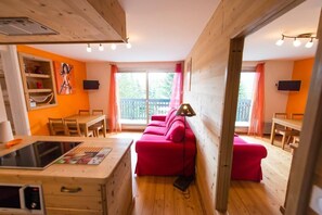 Une pièce confortable, aménagée comme un chalet, avec un intérieur en bois, un canapé rouge, une table à manger et un coin cuisine équipé d’un four à micro-ondes.