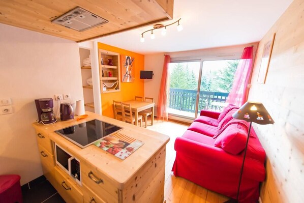 A compact living space with a kitchenette, a red sofa, and a dining area.