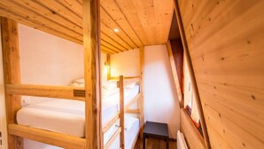 Una camera con un letto a castello in legno, un tavolino e una lampada fissata al muro.